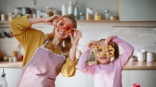 Funny Mom Child Holding Pepper Slices Peeping Through at Bright Kitchen Portrait