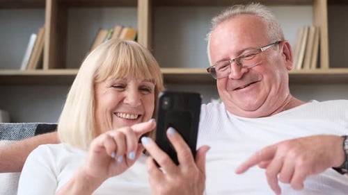 Elderly Couple Looking at Phone and Laughing Indoors