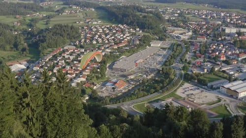 Tandem paraglider over forest hill with suburbs in background