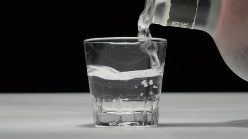 Transparent drink pouring into a glass, white background, close-up