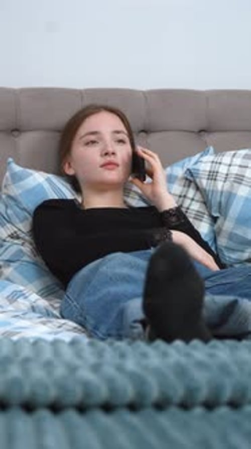 Young Woman Talking on Phone Lying on Bed