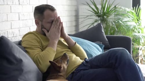 Man with Headache Resting on Couch with Dog