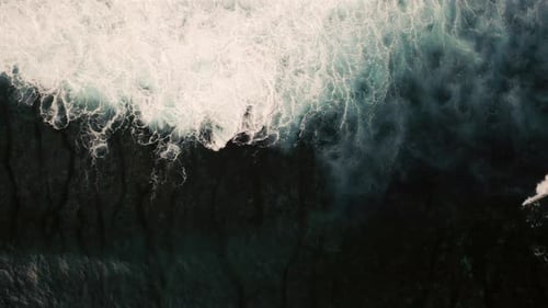 Aerial birds eye view of dramatic dark moody ocean water with white foaming waves breaking