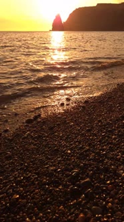 Sunset Ocean Beach Golden Sunset Over Calm Ocean Waves on a Pebble Beach with a Distant Mountain