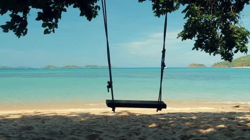 Nahaufnahme einer Seilschaukel, die an einer Palme an einem wunderschönen Strand mit weißem Sand und türkisfarbenem Wasser hängt