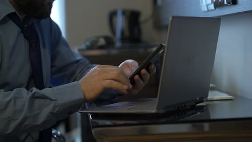 Young businessman analyzing data on laptop and smartphone at office table