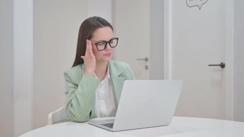 Woman Working on Laptop Rubbing Temple at Desk