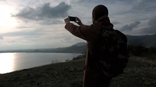 Person Filming Lake View with Smartphone at Sunset