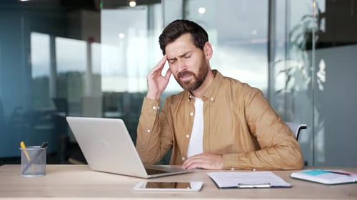 Businessman suffering from headache while working on laptop while sitting at the workplace in office