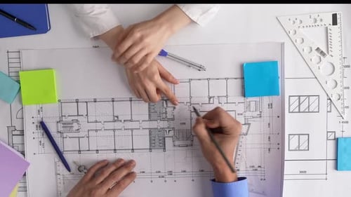 Hands Analyzing Architectural Blueprints in Office Setting