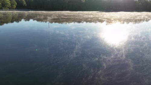 Aerial Drone View of Sunrise Fog Floating Over Calm Lake with Forest Reflections