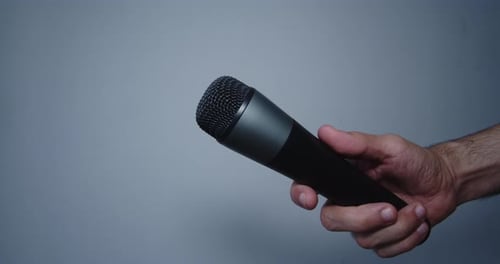 Musician holding a black microphone to sing in a room with white walls. 4K