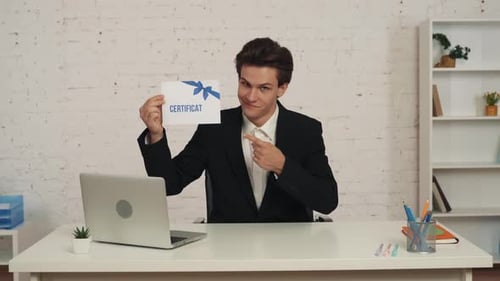 Medium Video of a Young Man Sitting at the Table in the Office Holding a Certificate in His Hands