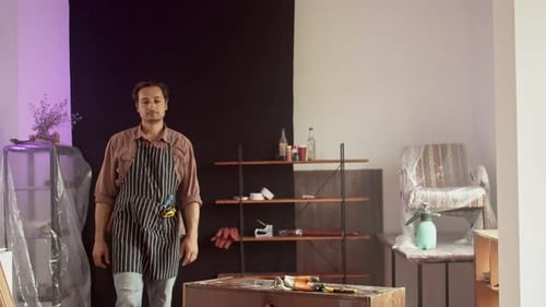Selbstbewusster erwachsener männlicher kaukasischer Möbelreparateur in einer speziellen Schutzschürze in einem Arbeitszimmer