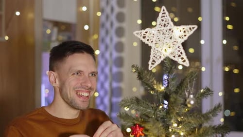 Man Decorates Christmas Tree with Festive Ornaments