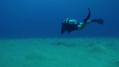 Lonely scuba diver with camera in his hands swims above sea bottom with sandy hills