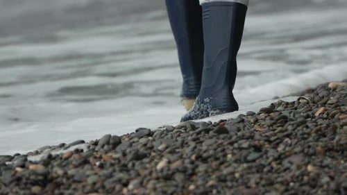 Rubber Boots Walking Pebble Beach As Ocean Waves Wash Over the Shoreline Traveler Exploring Nature