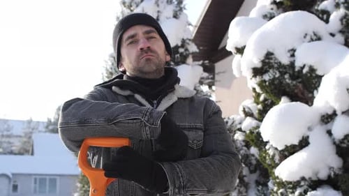 Man Leans on Shovel in Snowy Yard in Winter
