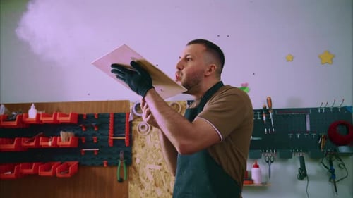 Carpenter Blowing Dust Off Wooden Board and Using Tablet