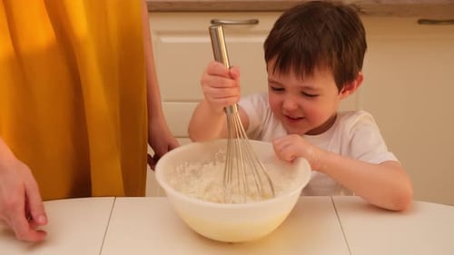 Little boy mixing dough in a bowl with a whisk helped by adult. Home kitchen cooking process. Family