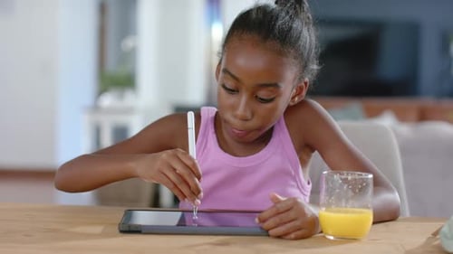 Female child of African descent responding to tablet, leaning and drawing with white stylus at home