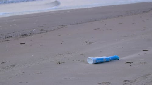 Blue plastic bottle on the beach, trash and waste litter on an empty Baltic sea white sand beach, en