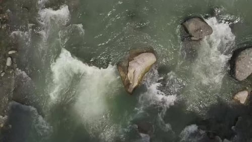 Strong water rapids flowing past large rocks in a river. Aerial shot, straight down.