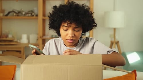 Young Woman Opens Box with Smartphone Indoors