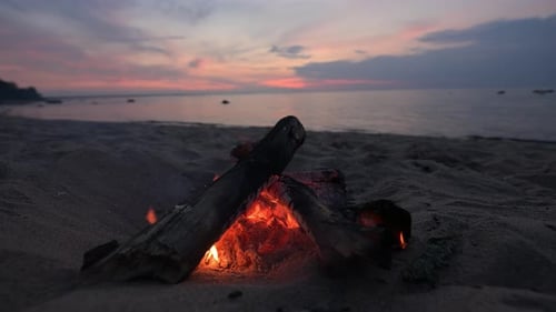 Lagerfeuer an einem Sandstrand bei Sonnenuntergang.