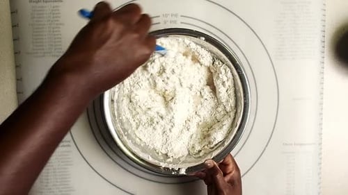 Overhead view of hands mixing all the ingredients to make the bread dough.