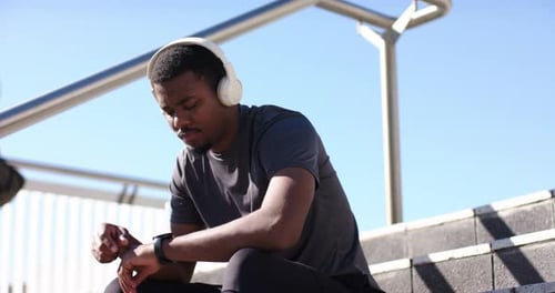 African American man tapping smartwatch to track run time during post-run break on concrete steps