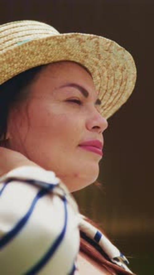 Une femme au chapeau de paille se reflète calmement au soleil, dégageant confiance et sérénité à travers elle