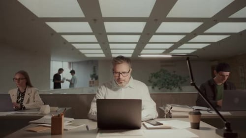 Empresário sênior focado trabalhando em laptop e mesa em escritório de plano aberto