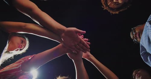 Diverse group of people placing hands together in center, symbolizing unity, strength, teamwork and