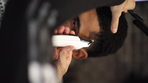 Nahaufnahme eines Friseurs, der den Haaransatz des Kunden mit einer Haarschneidemaschine vorsichtig formt und so für ein sauberes und sauberes Haar sorgt