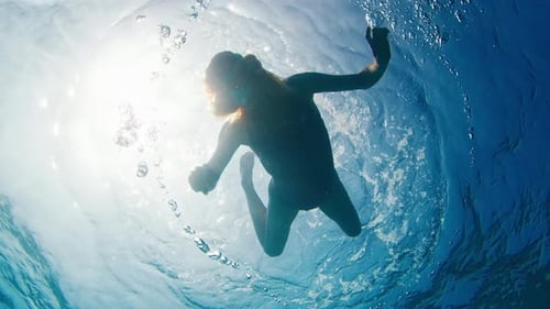 Fear of something on the depth. Woman swims in the sea and actively points to the bottom.