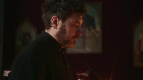 Priest Praying with Eyes Closed Holding Burning Candle in Church