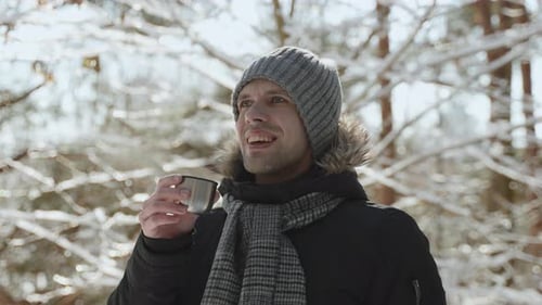 Man Drinks from Cup in Snowy Winter Forest
