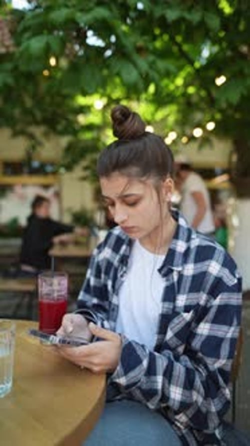 On a Summer Café Terrace a Stunning Young Woman with a Smartphone Enjoys a Cocktail