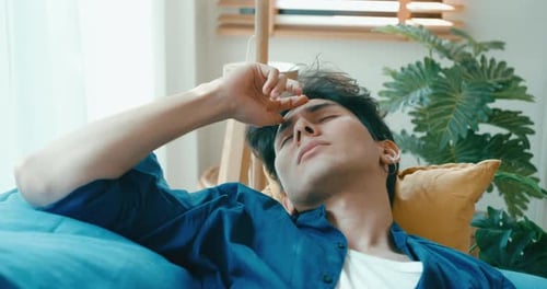 Close up tired exhausted young Asia male use laptop remote work asleep on couch sick.