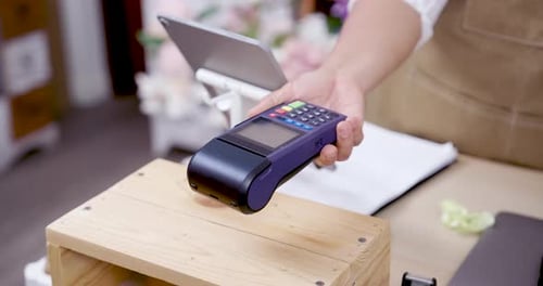 Credit card being inserted into POS terminal during cashless transaction in flower shop operated by