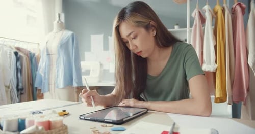 Asia female fashion designer with casual use digital tablet create new collection in her shop.