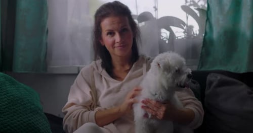 Woman Holding a White Dog Indoors on Couch