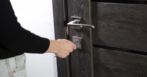 Woman opening wooden door with key indoors, closeup