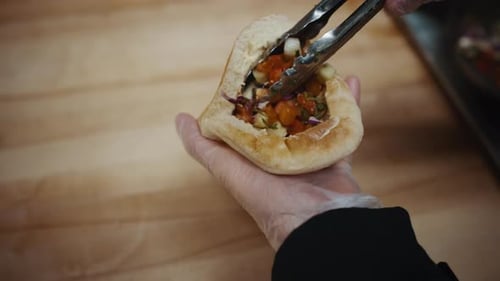 Person Preparing Pita Sandwich with Fresh Vegetables