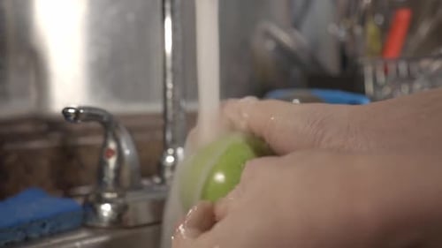 Washing The Green Apple Under The Running Water In The Kitchen Sink. -medium shot