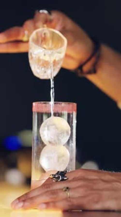 Pouring clear liquid into a cocktail glass with ice