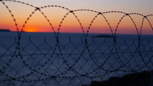 Razor wire reflecting sunset colors over calm ocean