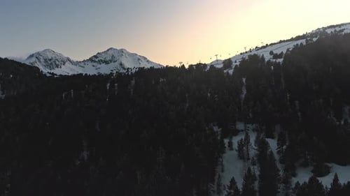 Aerial side view of ski lifts on an alpine snow mountain during golden hour