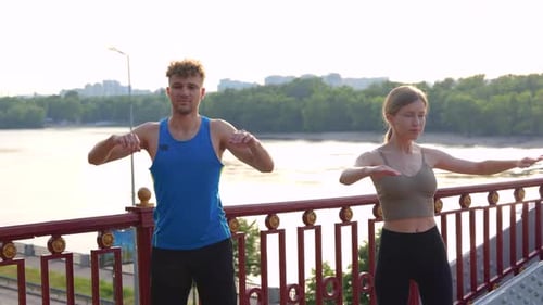 Young Couple in Sportswear Doing Stretching Exercises with Arms on the Bridge Outdoors in the City
